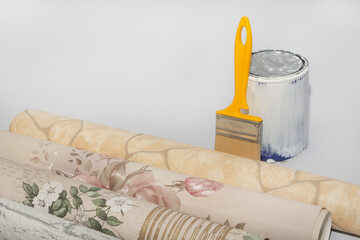 Multicolored wallpaper rolls, a can of paint, and a brush on a white background. Concept for a home or apartment renovation