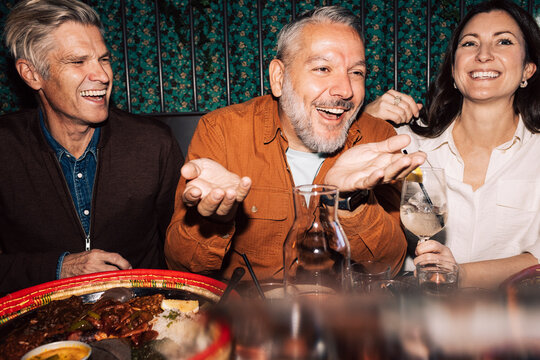 Happy mature man laughing while having fun with friends at dinner party