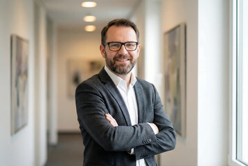 Obraz premium a professional man with a beard and glasses stands in a modern office corridor looking at the camera with a