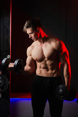 Muscular bodybuilder training biceps with dumbbells in red lighting.
