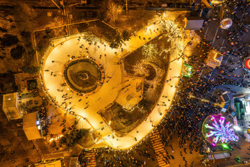 Aerial top-down view of a bustling city ice rink and festive market at night.