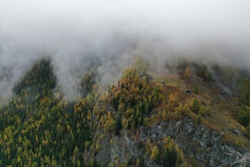 Aerial view of misty clouds swirling around the rugged, forested peaks, casting a serene yet dramatic spell over the landscape, Zermatt, Valais, Switzerland.