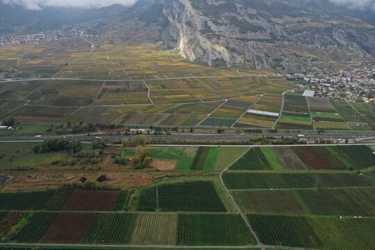 Aerial view of patchwork fields of vineyards and agricultural lands meet the rugged, rocky mountains, Zermatt, Valais, Switzerland.