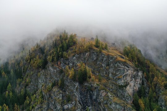 Aerial view of rugged cliffs dotted with vibrant autumn trees piercing through the ethereal mists, Zermatt, Valais, Switzerland.