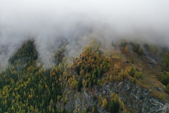 Aerial view of misty clouds swirling around the rugged, forested peaks, casting a serene yet dramatic spell over the landscape, Zermatt, Valais, Switzerland.