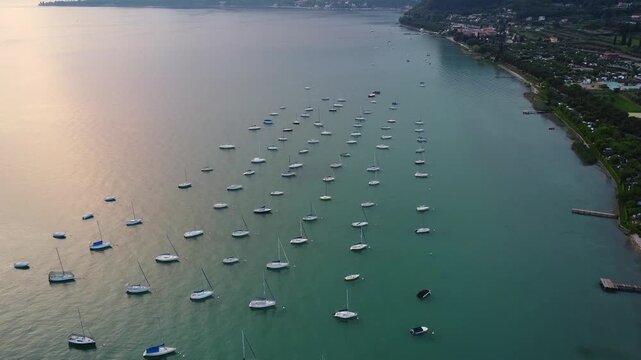 Top-down drone video of white motor yachts anchored in perfect geometric rows on Lake Garda, Italy, near Bardolino, showcasing symmetry, calm water, luxury boating, and elegant lakeside scenery