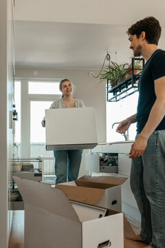 Smiling young woman carrying cardboard box unpacking stuff with boyfriend at new house