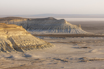 View of sun-kissed, layered cliffs and plateaus rise from the arid landscape, contrasting textures and earthy tones, Bozhira, Mangystau Region, Kazakhstan.