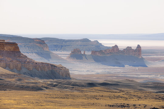 View of layered mesas casting shadows on the arid land under a hazy sky, creating a serene yet dramatic scene, Bozhira, Mangystau Region, Kazakhstan.