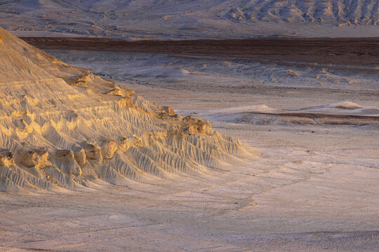 View of sunlit, eroded cliffs casting shadows over the arid landscape, revealing layers of earth in a textured tableau, Bozhira, Mangystau Region, Kazakhstan.