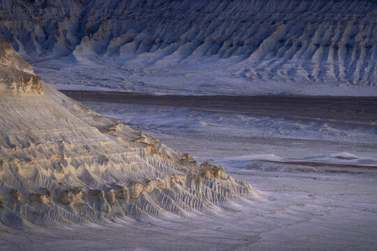 View of layered cliffs casting shadows across the arid landscape, showcasing the raw beauty and geological formations, Bozhira, Mangystau Region, Kazakhstan.