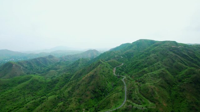 4K Aerial shot of road passing through Aravalli hills and clouds in sky at Rayta in Udaipur, Rajasthan, India. Monsoon clouds and green hills of Rayta. Tourism and holidays background. 