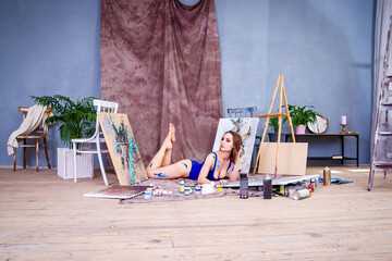 Beautiful young female artist in art studio surrounded by paintings