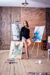 Beautiful young female artist in art studio surrounded by paintings