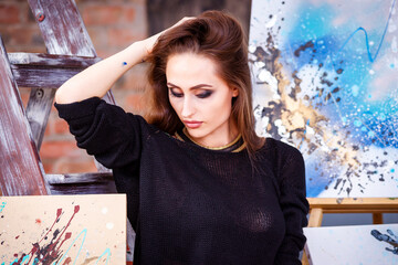 Beautiful young female artist in art studio surrounded by paintings