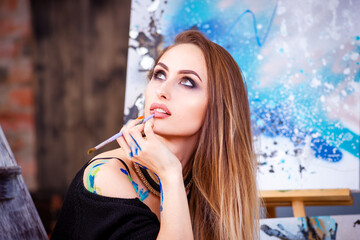 Beautiful young female artist in art studio surrounded by paintings