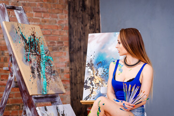 Beautiful young female artist in art studio surrounded by paintings