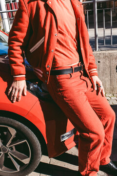 Young man in red clothing sitting on car bonnet at sunny day