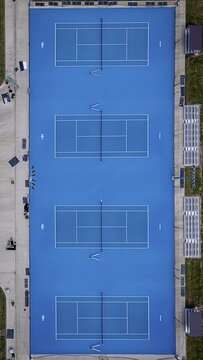 Aerial view of four vibrant blue tennis courts, crisp white lines cutting through the cerulean expanse, framed by concrete pathways, Lovedale, New South Wales, Australia.
