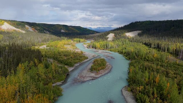 Aerial view of a winding river cutting through a dense forest with contrasting light and shadows, creating a dramatic landscape, Copper Center, Alaska, United States.