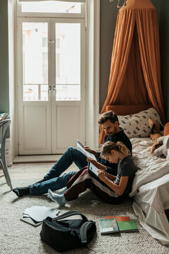 Father helping daughter in doing homework while sitting on carpet near sofa at home
