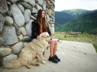 Obraz premium Girl sitting with a large dog beside a stone wall in a mountain landscape, outdoors, enjoying tranquil nature and a scenic valley during a calm hike in fresh mountain air