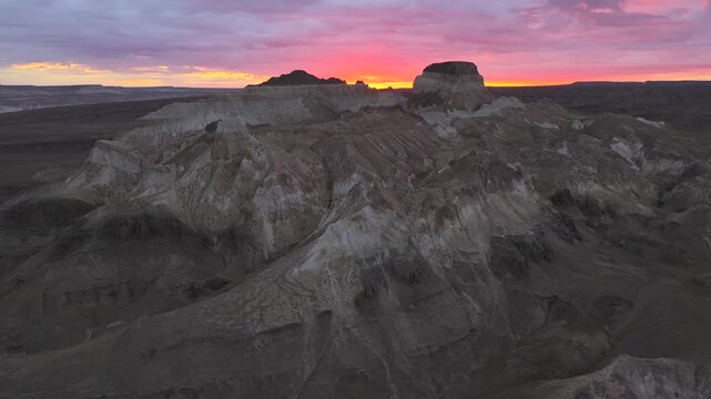 Aerial view of the Shetpe Airakty Castle under the pink sky, where beige rocky outcrops create a stark contrast with the dark, flat plains, Shetpe, Mangystau Region, Kazakhstan.