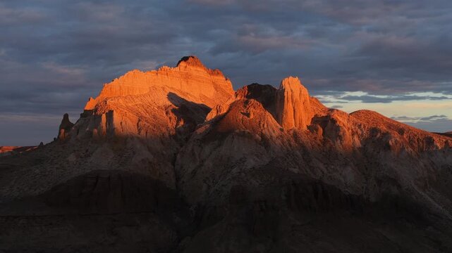 Aerial view of Airakty Castle basking in the warm glow of the setting sun contrasting with the dark shadows and cloudy sky, Shetpe, Mangystau Region, Kazakhstan.
