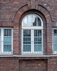 Obraz premium Brick wall featuring barred window with decorative glass panes in urban setting during cloudy day