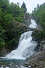 Fototapeta premium Experience the raw power and refreshing serenity of a multi-tiered waterfall cascading through a dense, vibrant green forest. A perfect scene for themes of nature, purity, and peaceful discovery