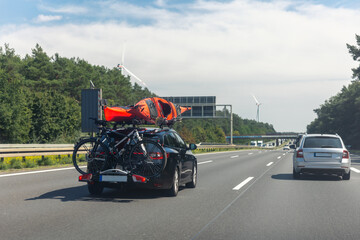 Back view modern black family wagon van car with mounted roof kayak and bike tail carrier driving european highway road against blue sky summer day. Lifestyle travel adventure trip journey concept