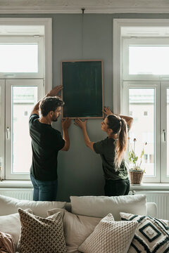Couple adjusting picture frame on wall at new home