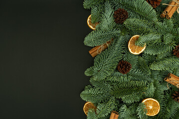 Evergreen Fir Branches with Cones, Dried Orange Slices and Cinnamon Sticks on Dark Background with Copy Space