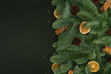 Evergreen Fir Branches with Cones, Dried Orange Slices and Cinnamon Sticks on Dark Background with Copy Space