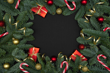 Evergreen Fir Branches with Red Gift Boxes, Christmas Ornaments and Candy Canes on Dark Background with Copy Space