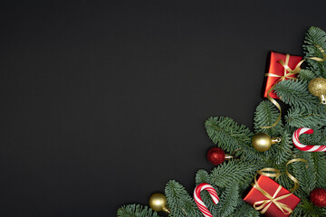 Evergreen Fir Branches with Red Gift Boxes, Christmas Ornaments and Candy Canes on Dark Background with Copy Space