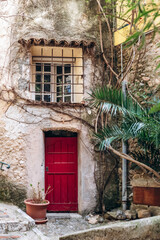 Fototapeta premium Old stone house facade with red wooden door and window in the historic village Roquebrune Cap Martin
