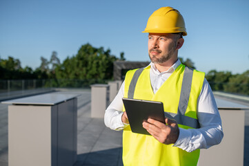 Engineer wearing helmet and safety vest inspecting solar panels with tablet