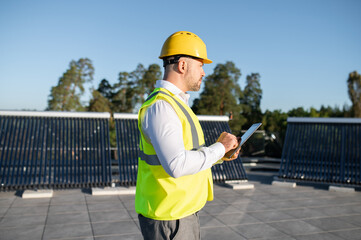 Engineer in protective vest analyzing solar energy installation with gadget