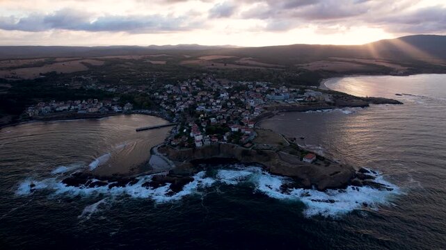 Aerial view of Ahtopol's charming cityscape where terracotta roofs meet the rugged coastline, as waves crash against the rocks at sunset, Ahtopol, Burgas, Bulgaria.