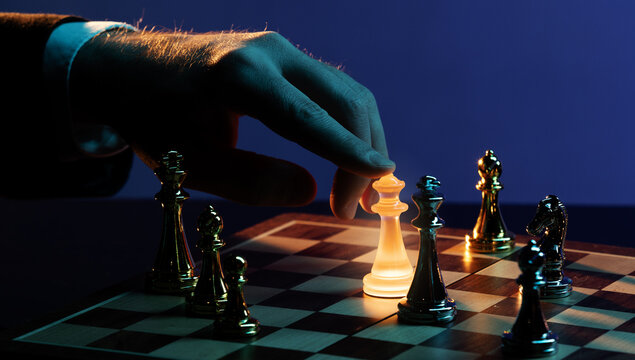 Hand moving glowing golden chess king across board. Concept of premium business strategy, gambling psychology, leadership control, risk driven decisions and competitive planning.