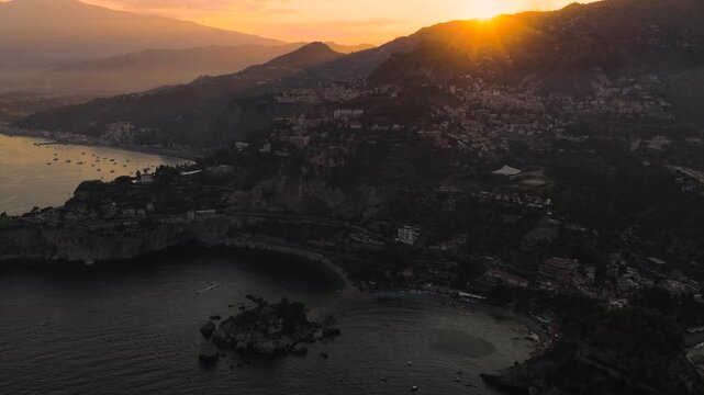 Aerial view of the dramatic coastline meeting the Ionian Sea, with Isola Bella island bathed in the warm glow of sunset, Isola Bella, Sicily, Italy.