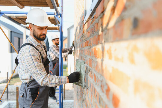 Construction workers bricklaying house wall, applying mortar