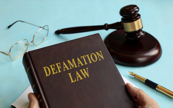Hand Holding Defamation Law Book with Judge Gavel and Glasses