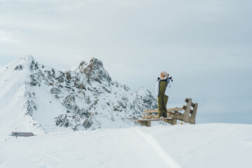 Woman enjoying winter mountain landscape view from bench in klosters