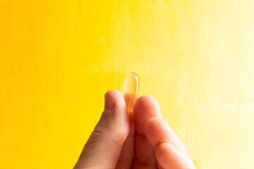 Hand holding translucent fish oil vitamin d capsule