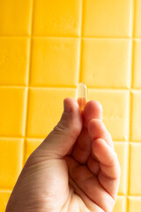 Hand holding nutritional supplement capsule on yellow background
