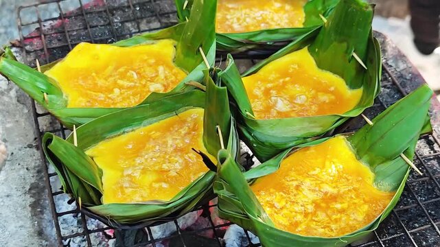 Close-up of Khai Pam, a Northern Thai grilled egg dish prepared with eggs and sauce in banana leaf containers at a local street food market.