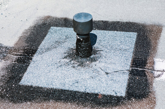 Flat roof vent is installed on a rooftop. Seal looks effective around the base. Bitumen roof penetration flashing detail, showing granular surfacing