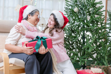 A young woman gives a red gift box to an older woman for Christmas